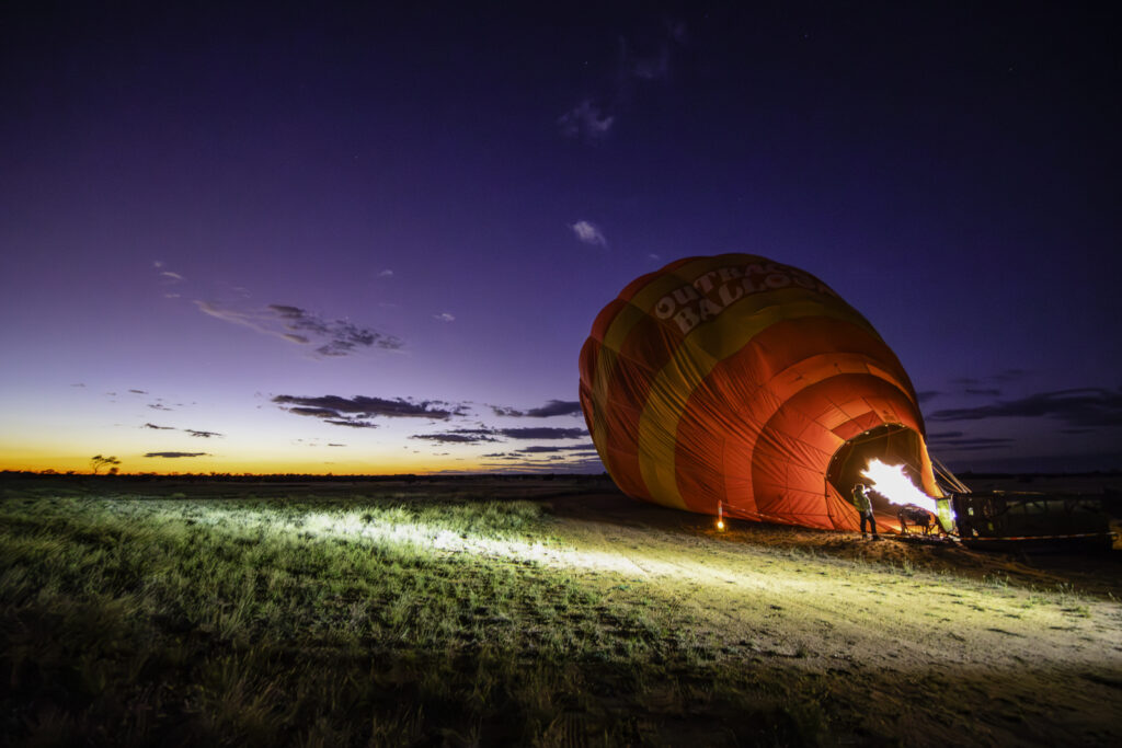 Experience the magic of sunrise with Outback Ballooning in Alice Springs! Watch the hot air balloon fill up with the powerful burners roaring, as the first light of dawn paints the sky. Visit www.outbackballooning.com.au to book your unforgettable journey.