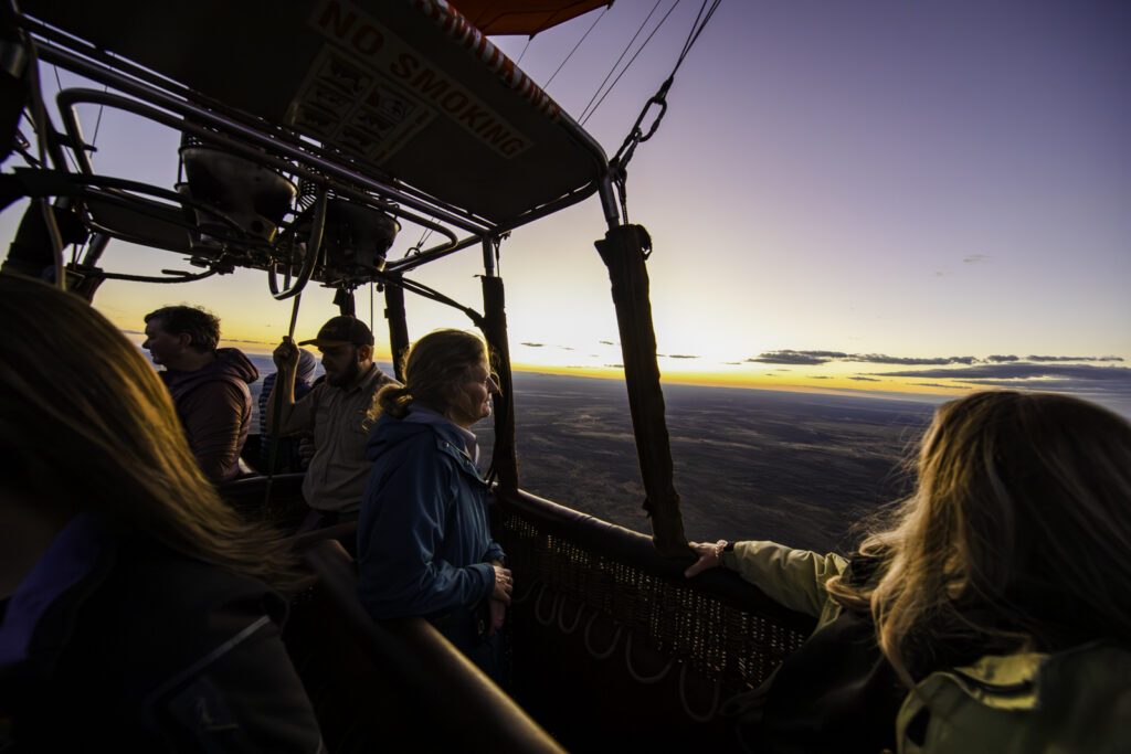 Experience the peaceful beauty of Alice Springs with Outback Ballooning. Witness a woman silhouetted against the dawn sky as she contemplates the breathtaking nature around her from the balloon's basket. Discover the serenity of the Australian Outback from a unique perspective with www.outbackballooning.com.au.